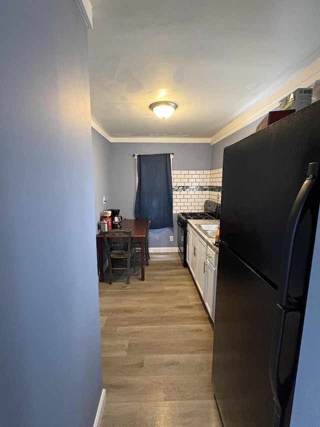 kitchen featuring white cabinets, ornamental molding, backsplash, black appliances, and light wood finished floors