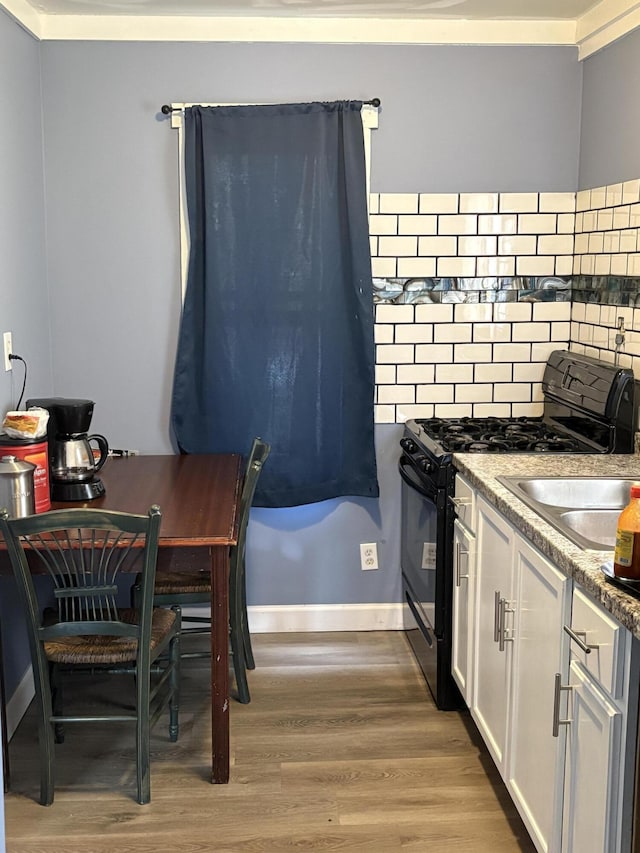 kitchen with decorative backsplash, light wood-style floors, gas stove, white cabinetry, and baseboards