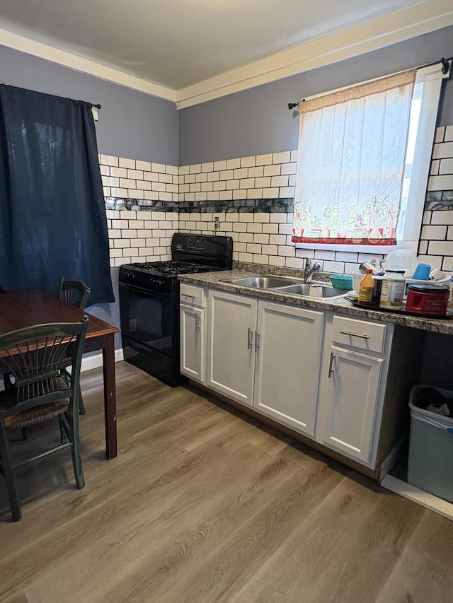 kitchen with light wood finished floors, dark countertops, backsplash, black gas stove, and a sink