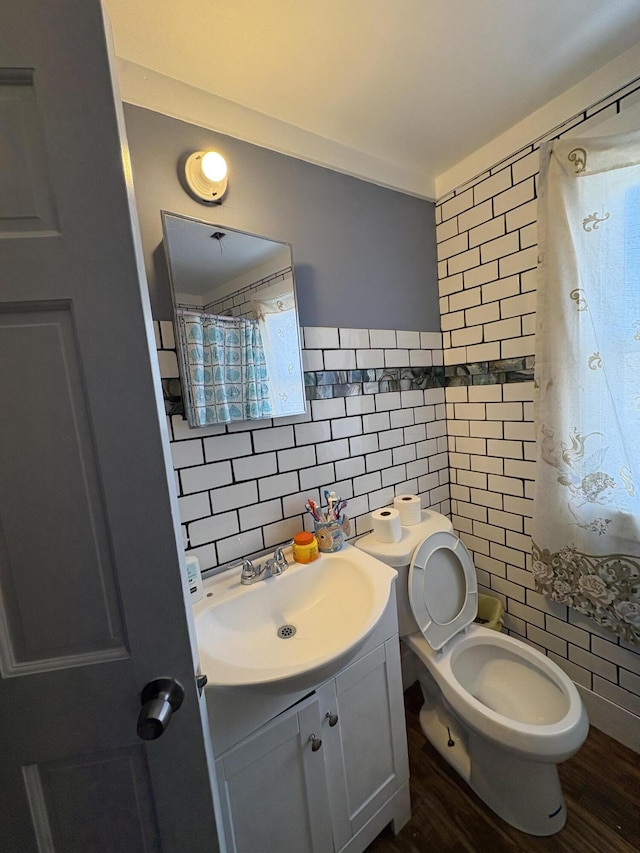 bathroom with toilet, wood finished floors, tile walls, and vanity