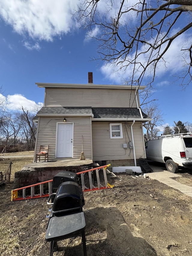 rear view of property with a shingled roof and a chimney