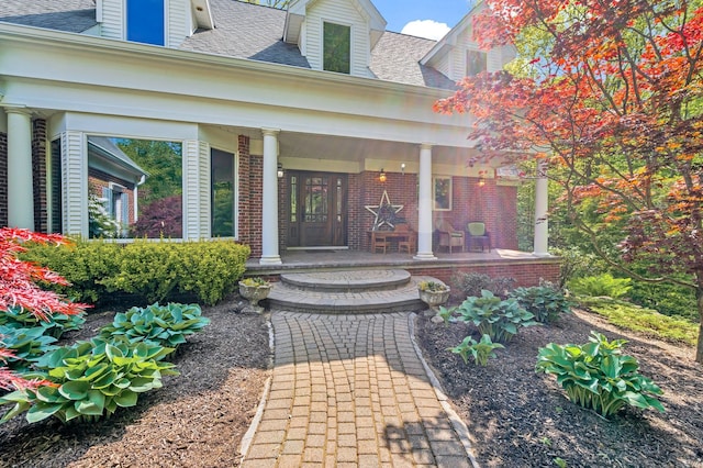 doorway to property with covered porch, brick siding, and a shingled roof