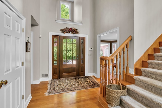 entryway featuring baseboards, visible vents, stairway, wood finished floors, and a high ceiling