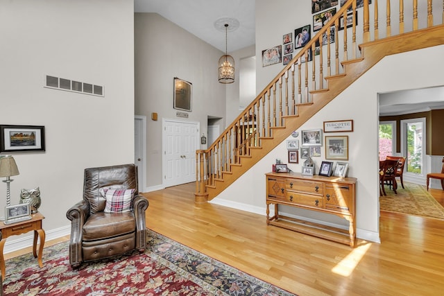 foyer with a chandelier, visible vents, wood finished floors, high vaulted ceiling, and stairs