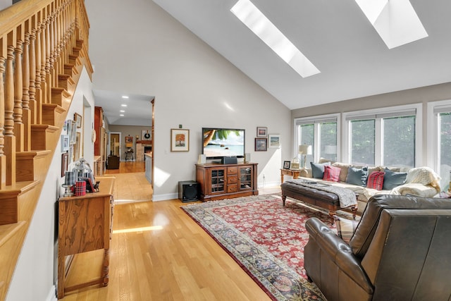 living room featuring a skylight, light wood-style flooring, high vaulted ceiling, a lit fireplace, and baseboards