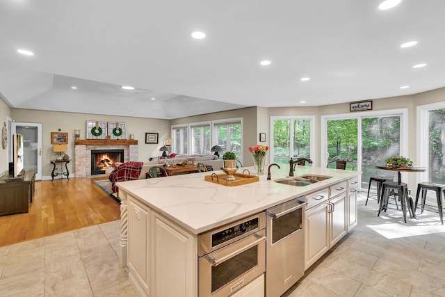 kitchen featuring a warm lit fireplace, open floor plan, a sink, and stainless steel oven