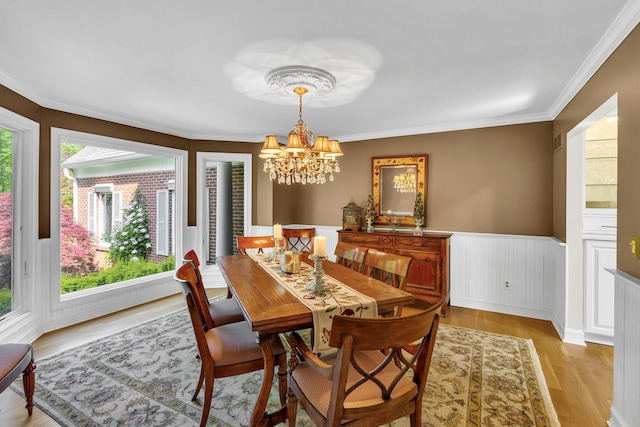 dining space featuring ornamental molding, wainscoting, an inviting chandelier, and light wood-style floors