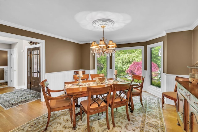 dining room with light wood-style flooring, crown molding, a notable chandelier, and wainscoting