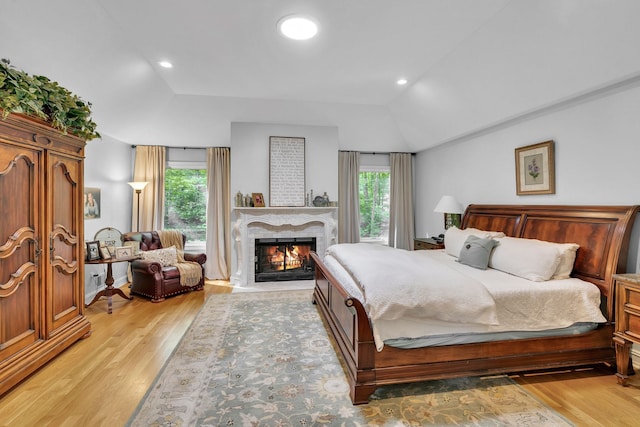 bedroom with a fireplace with flush hearth, lofted ceiling, light wood-style floors, and recessed lighting