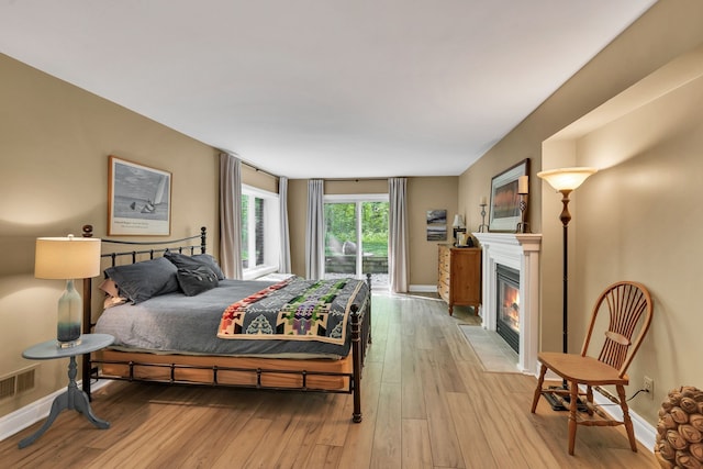 bedroom featuring visible vents, baseboards, a fireplace with flush hearth, access to outside, and light wood-style floors