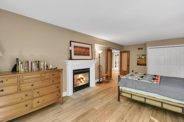 bedroom featuring visible vents, baseboards, a fireplace with flush hearth, light wood-style flooring, and a closet