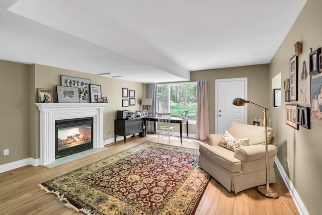 living room with a fireplace with flush hearth, baseboards, and wood finished floors