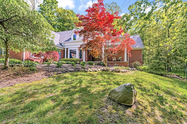 view of front of home featuring brick siding, roof with shingles, and a front yard