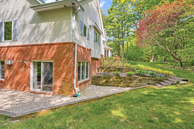 view of side of home featuring a patio, a lawn, and brick siding