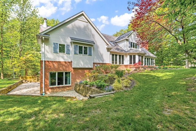 back of house featuring a yard, a chimney, a patio, and brick siding