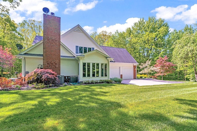 back of property with a garage, concrete driveway, a yard, and a chimney