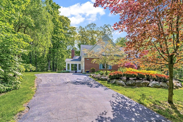 view of front of property featuring aphalt driveway, a front lawn, a chimney, and brick siding