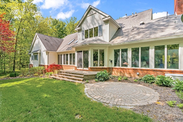 rear view of house with a patio, brick siding, a sunroom, a yard, and roof with shingles