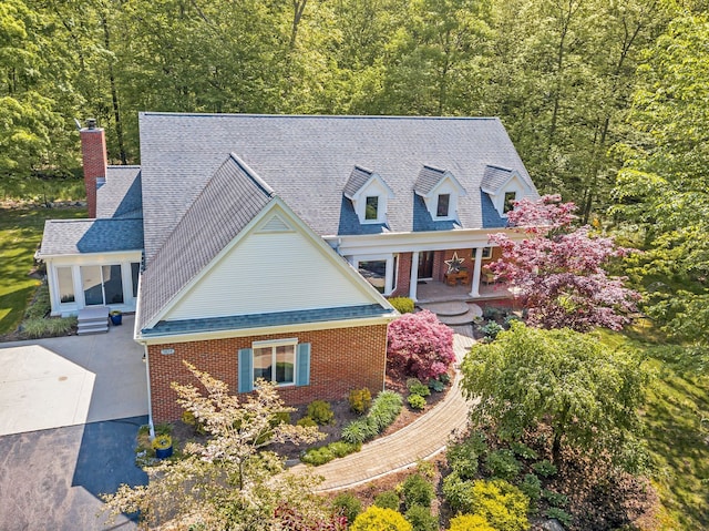 view of front of house featuring driveway, brick siding, a chimney, and a shingled roof