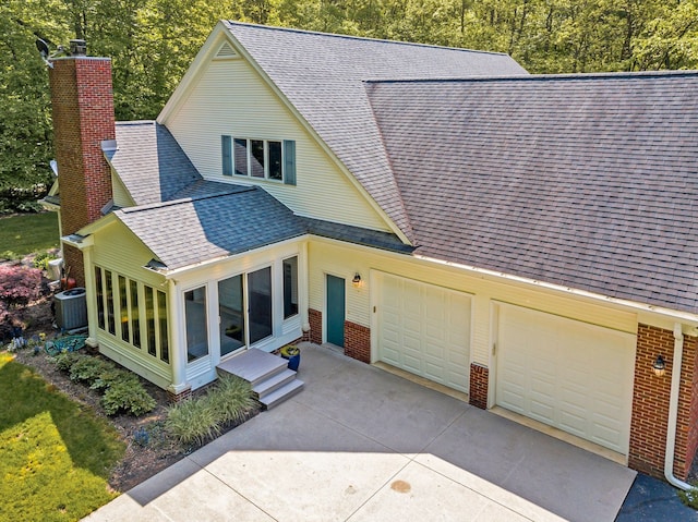 view of front facade featuring central air condition unit, roof with shingles, a chimney, and brick siding