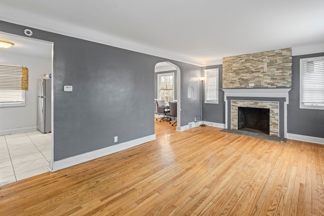 unfurnished living room featuring arched walkways, a fireplace, baseboards, ornamental molding, and light wood finished floors