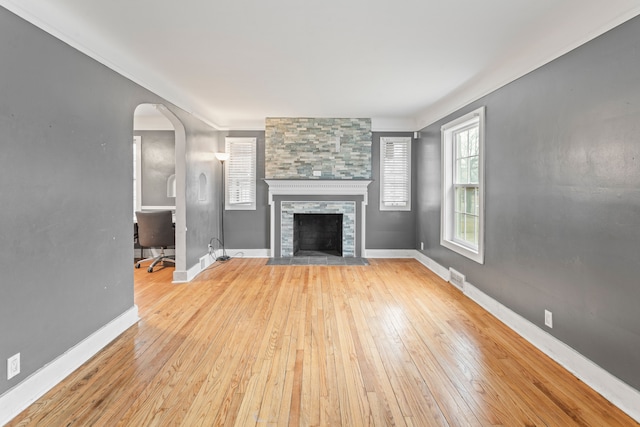 unfurnished living room with a stone fireplace, wood-type flooring, visible vents, and baseboards