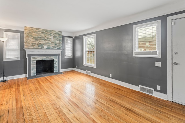 unfurnished living room featuring hardwood / wood-style flooring, baseboards, visible vents, and a stone fireplace