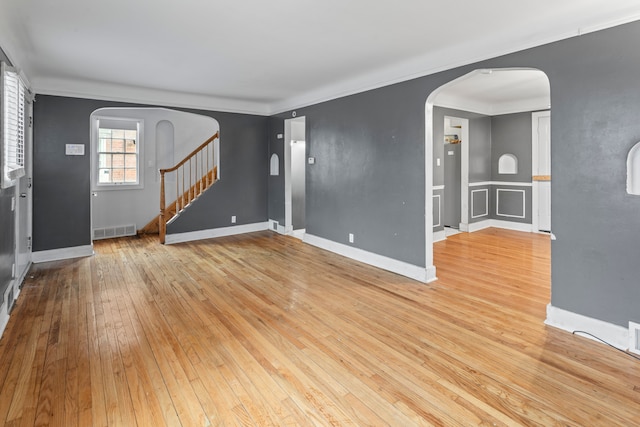 unfurnished living room with arched walkways, hardwood / wood-style flooring, visible vents, ornamental molding, and stairway