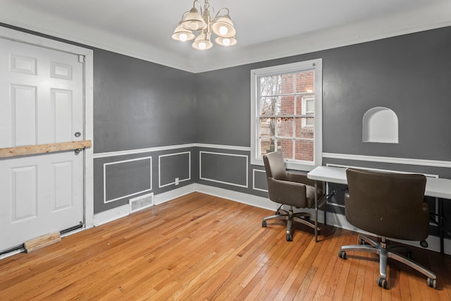 office featuring a notable chandelier, visible vents, a decorative wall, wainscoting, and hardwood / wood-style flooring