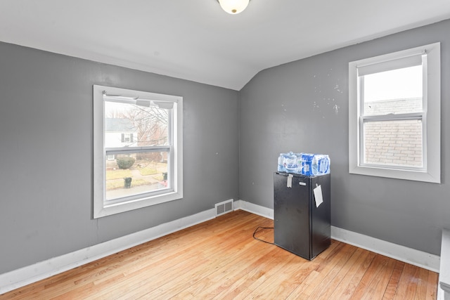 empty room with visible vents, wood-type flooring, lofted ceiling, and a wealth of natural light