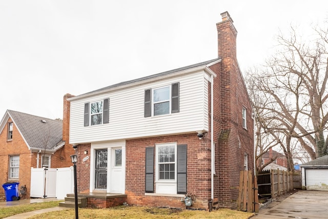 colonial-style house with brick siding, fence, a chimney, and an outdoor structure