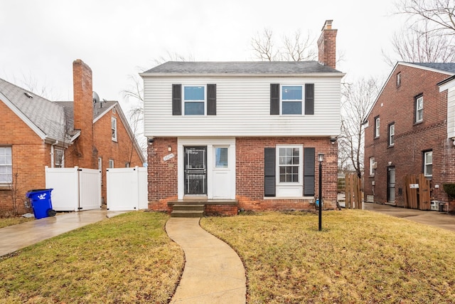 colonial-style house featuring a gate, brick siding, fence, and a front lawn