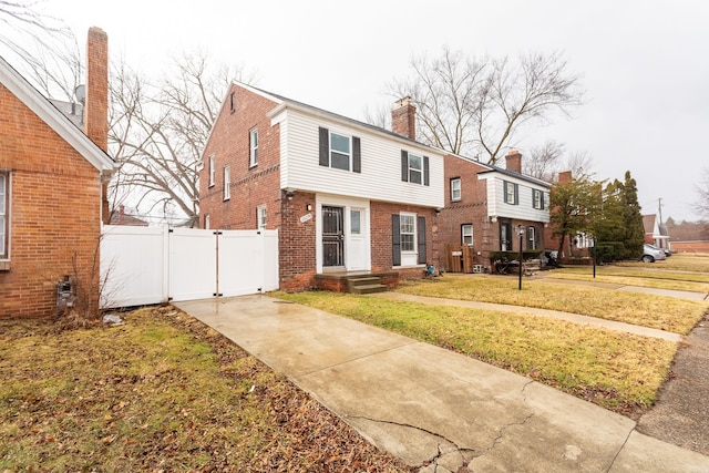 colonial inspired home featuring brick siding, a front yard, fence, and a gate