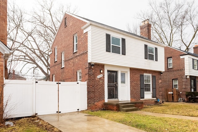 colonial house featuring brick siding, a chimney, fence, and a gate