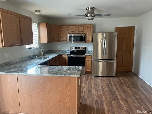 kitchen featuring dark wood-type flooring, a sink, light stone counters, appliances with stainless steel finishes, and a peninsula