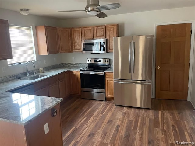 kitchen with a sink, stainless steel appliances, light stone counters, and dark wood-style floors