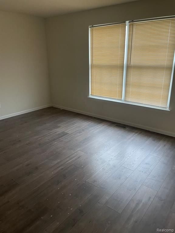 spare room featuring visible vents, baseboards, and dark wood-type flooring