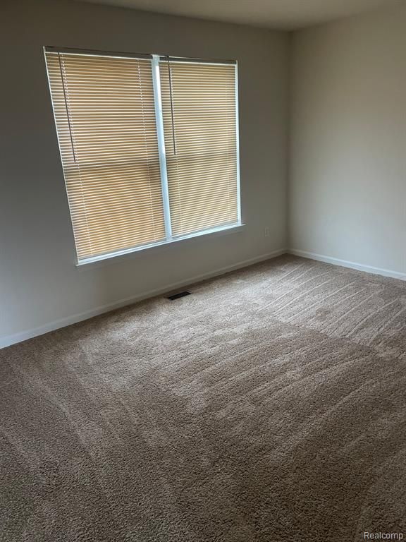 carpeted empty room with visible vents and baseboards