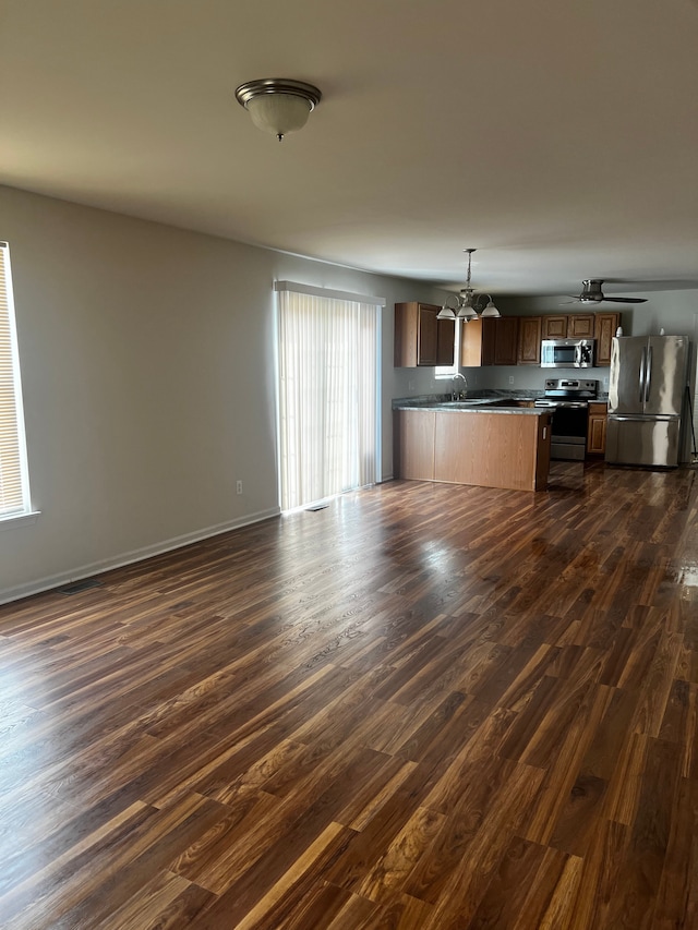 kitchen with a peninsula, appliances with stainless steel finishes, open floor plan, and dark wood finished floors