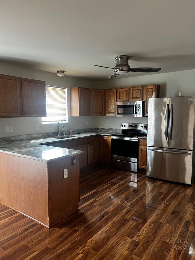 kitchen with a sink, dark wood-style floors, a peninsula, appliances with stainless steel finishes, and ceiling fan