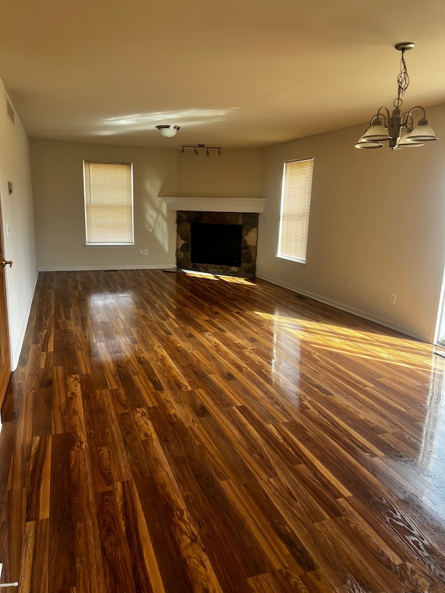 unfurnished living room featuring a stone fireplace, an inviting chandelier, dark wood-style floors, and baseboards