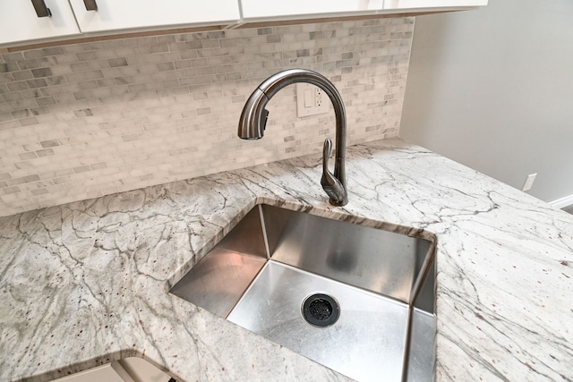 room details with a sink, light stone counters, backsplash, and white cabinetry