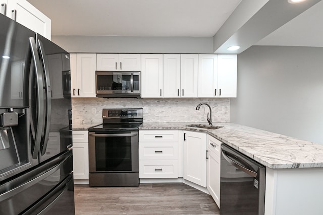 kitchen with light stone countertops, a peninsula, a sink, decorative backsplash, and stainless steel appliances