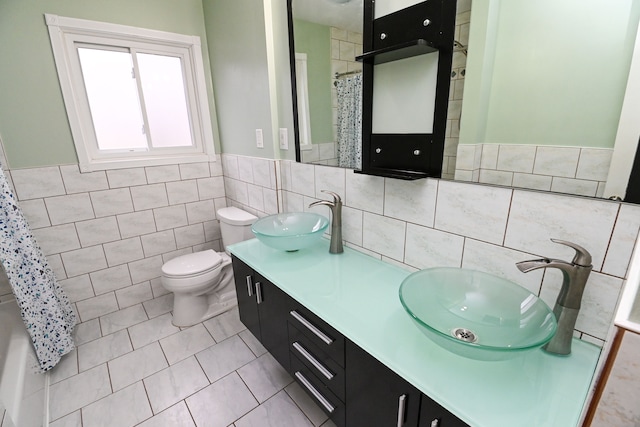 full bath with tile walls, toilet, double vanity, and a sink