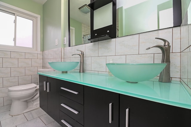 bathroom with tile walls, toilet, double vanity, and a sink