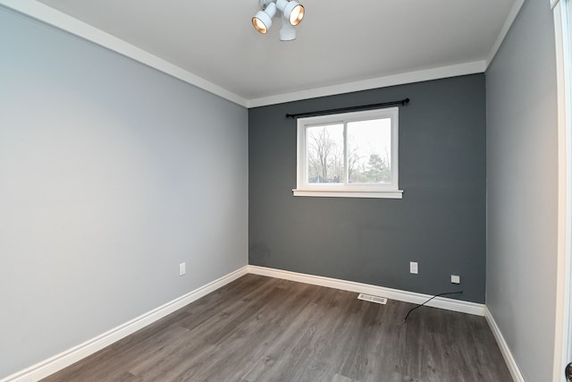 spare room with visible vents, baseboards, wood finished floors, and ornamental molding