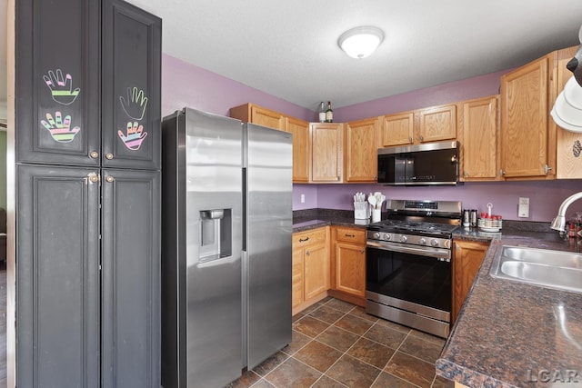 kitchen with dark countertops, stone finish floor, stainless steel appliances, and a sink