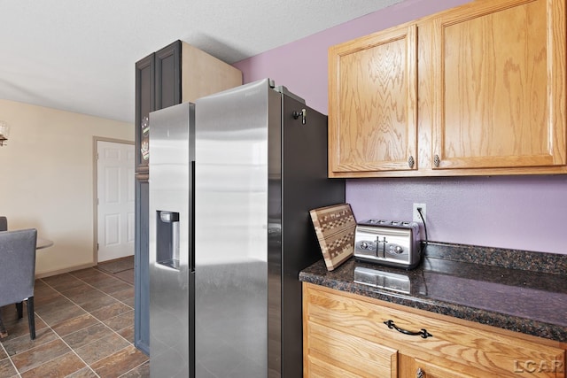 kitchen with dark stone counters, baseboards, stone finish floor, stainless steel fridge with ice dispenser, and light brown cabinets