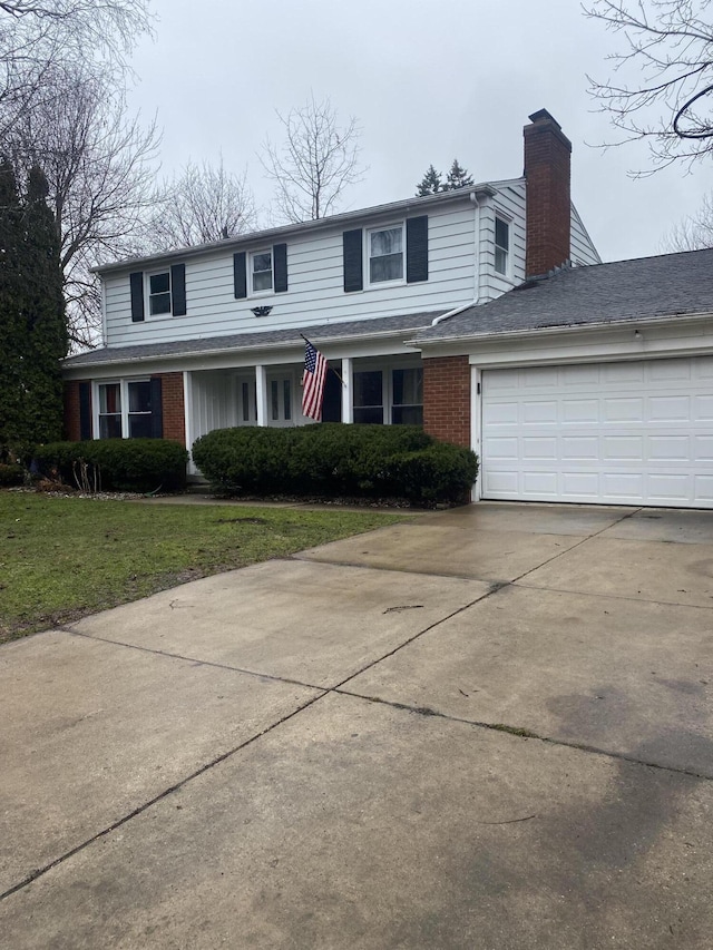 traditional-style house with brick siding, concrete driveway, a front yard, a chimney, and a garage