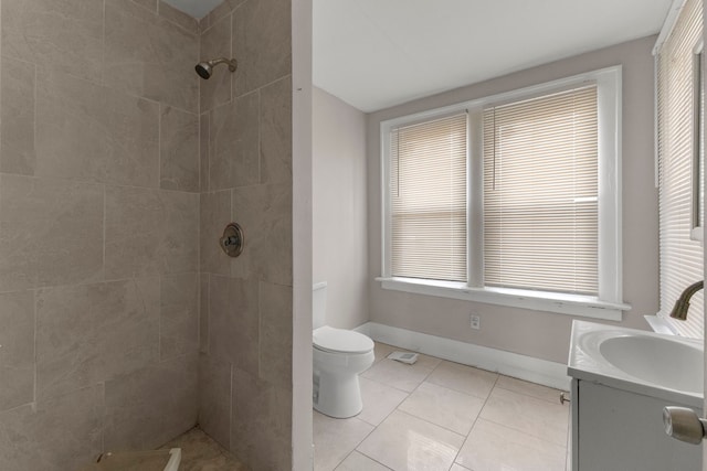 bathroom with toilet, vanity, baseboards, tiled shower, and tile patterned floors